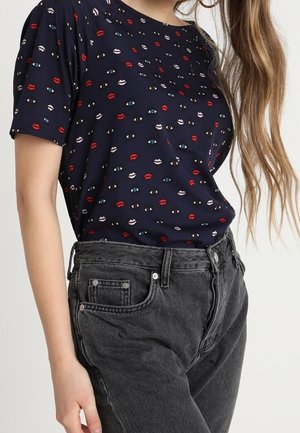 Granatowy top z krótkim rękawem z wesołym wzorem czerwonych ust i kolorowych oczu. Połączony z wysokim stanem czarnych dżinsów.