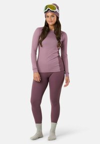 Zestaw termiczny w kolorze mauve z prążkowanej dzianiny, składający się z bluzki z długim rękawem i legginsów. Model ma na sobie szare skarpetki z dzianiny oraz pasującą czapkę z goglami.