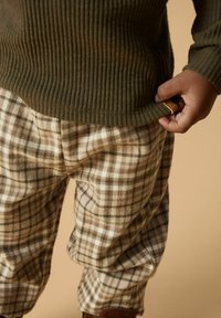 Groene geribde trui met een bruine en crèmekleurige geblokte broek, met een losse pasvorm en een zichtbaar label bij de taille. Zachte textuur, casual ontwerp.