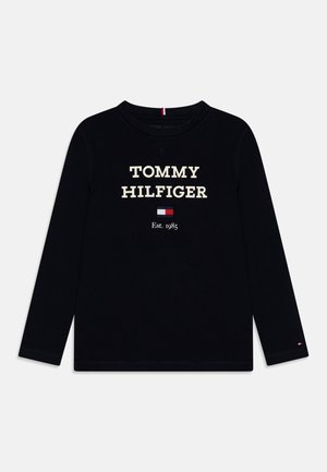Schwarzes Langarm-T-Shirt mit der Aufschrift "TOMMY HILFIGER" in cremefarbener Schrift, einem kleinen Logo-Flag und "Est. 1985" unter dem Text. Aus weichem Baumwollstoff.