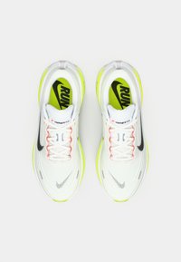 Chaussures de course Nike avec un dessus en maille blanche, un logo noir, des accents jaune fluo, des lacets orange et des semelles vertes avec le texte "RUN".