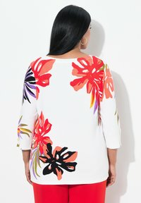 Maglione bianco con vivaci motivi floreali in rosso, arancione, viola e nero. Taglio a tre quarti di manica e scollatura rotonda.
