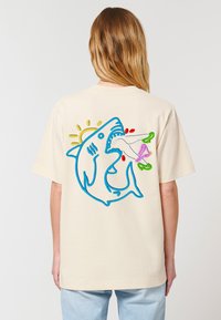 Cremefarvet bomulds-t-shirt med en blå hajgrafik på ryggen, med farverige accenter i grøn, pink og rød samt en sol-detalje.