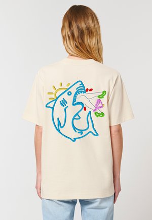 Cream-colored cotton t-shirt featuring a blue shark graphic on the back, with colorful accents of green, pink, and red, plus a sun detail.
