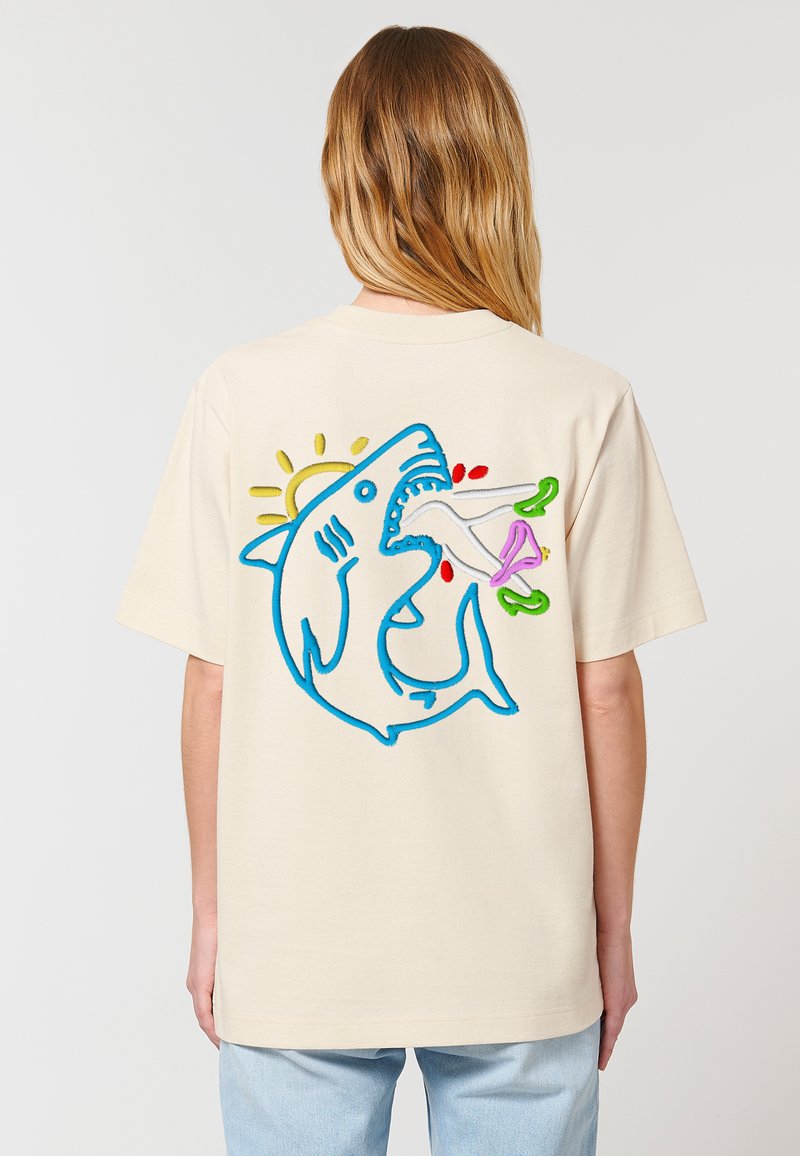 Cremefarvet bomulds-t-shirt med en blå hajgrafik på ryggen, med farverige accenter i grøn, pink og rød samt en sol-detalje.