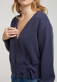 Pull enveloppant bleu marine en tricot texturé, avec un décolleté en V plongeant, des manches longues et un lien à la taille.