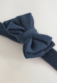 Jūras zilā adīta tauriņu kaklasaite ar teksturētu virsmu, kurai ir liels mezgls un cieta josta. Materiāls izskatās mīksts un elastīgs.
