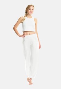 Top corto bianco e pantaloni bianchi morbidi realizzati in un tessuto leggero, con una texture liscia e due tasche frontali.
