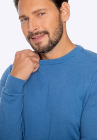 Hellblau gestrickter Pullover mit Rundhalsausschnitt und gerippten Bündchen. Das Material wirkt weich und der Schnitt liegt eng an den Schultern an.