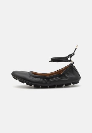 Ballerines en cuir noir avec un bout arrondi, des détails froncés autour de l'ouverture et une semelle en caoutchouc flexible. Lanières à la cheville.