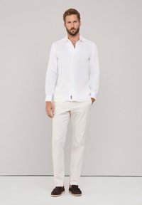 Chemise bl blanche à col pointu, associée à un pantalon crème et des mocassins marron foncé. Texture lisse et design simple.