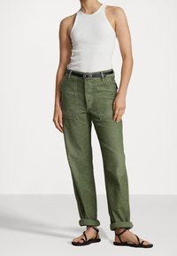 Olijfgroene cargobroek met een relaxte pasvorm, voorzakken en opgerolde boorden, gecombineerd met een aansluitend witte tanktop en een zwarte riem. Platte sandalen.