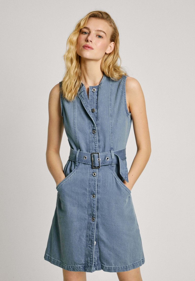 Abito senza maniche in denim azzurro chiaro, con chiusura a bottoni frontale, vita con cintura e tasche laterali; presenta una gonna leggermente svasata e colletto.
