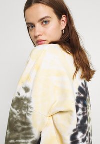 Sweatshirt oversize con motivo tie-dye in giallo, nero e grigio. Realizzato in cotone morbido, con una vestibilità comoda e scollatura rotonda.