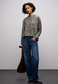 Leopardmönstrad tröja i beige och svart, ihop med blå vida jeans. Modellen håller en brun väska och visar upp en avslappnad outfit.
