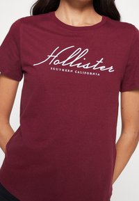 Camiseta de algodón burdeos de manga corta, con el logo en cursiva blanca "Hollister" y el texto "Southern California" debajo.