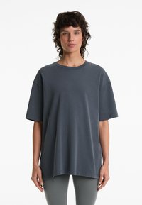 Tmavě šedé oversized tričko vyrobené z bavlny, s krátkými rukávy, kulatým výstřihem a volným střihem. Hladká textura bez viditelných vzorů.