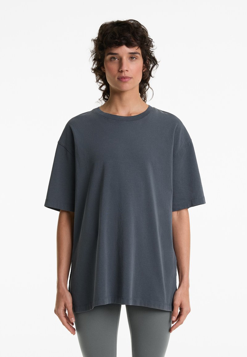 Tmavě šedé oversized tričko vyrobené z bavlny, s krátkými rukávy, kulatým výstřihem a volným střihem. Hladká textura bez viditelných vzorů.