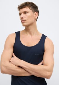 Tmavomodré rebrované tielko s okrúhlym výstrihom a malým vyrazeným logom na ľavej strane hrudníka. Materiál pôsobí mäkko a pružne.