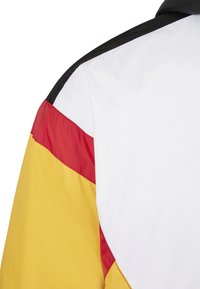Gros plan d'une veste montrant une manche à blocs de couleurs noire, blanche, rouge et jaune.