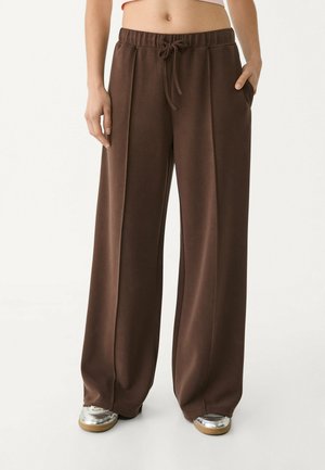 Bruine wijde broek van zacht materiaal met een elastische tailleband, koord en zijzakken. Heeft een gladde textuur en een ontspannen pasvorm.