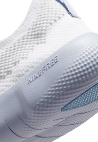 Białe tekstylne buty sportowe z jasnoniebieską gumową podeszwą, z teksturowanym wzorem i wytłoczonym logo "Nike Free" z boku.