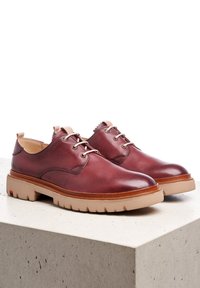 Chaussures en cuir bordeaux à bouts ronds, avec quatre œillets et semelle en caoutchouc beige. Elles présentent une semelle intérieure contrastante en tan et une languette.