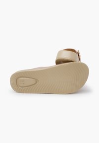 Beige sandals with a smooth, glossy strap and textured insole. The rubber sole features a wave pattern for grip and flexibility.