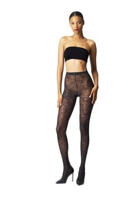 Kvinde iført sort strapless top, mønstrede gennemsigtige sorte strømpebukser og sorte højhælede sko, som står med den ene hånd på låret.