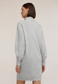 Abito maglione sovradimensionato grigio chiaro con collo alto, spalle scese, polsini a coste e un motivo in maglia testurizzata.