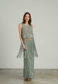 Groene fringed jurk gemaakt van gaas materiaal met een cropped top en lange rok. Beschikt over een textuurpatroon en geweven ontwerp.