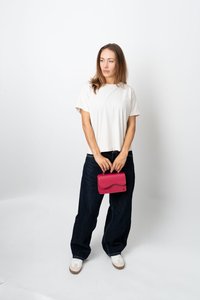 Kvinna i vit t-shirt och mörka vida jeans som håller en liten rosa handväska, stående mot en enkel vit bakgrund.