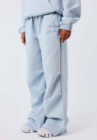 Pantalons de survêtement bleus clairs en tissu doux avec une taille élastique. Présente des accents brodés et des jambes larges. Associés à des baskets blanches.