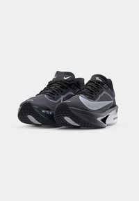 Chaussures de sport noires et grises en matériaux en maille et en caoutchouc, semelles texturées, avec un logo discret sur la languette et le côté.