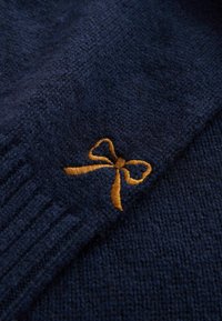 Maglione blu navy scuro in lana strutturata, con un dettaglio a fiocco ricamato in oro sul davanti. Orlo ribattuto verticale nella parte inferiore.