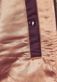 Gros plan d’un tissu marron clair brillant avec une bande verticale marron foncé présentant un seul bouton pression rond noir.