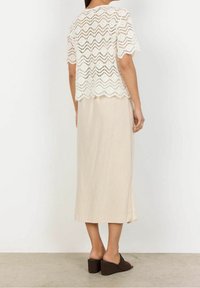 Bílé, krátké háčkované tričko s cik-cak vzorem; vrstvené přes béžovou sukni do kolen se bočním rozparkem; hnědé sandály na podpatku.