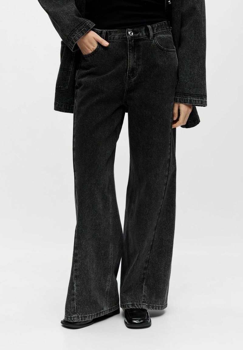 High-waisted, flared black denim jeans with front pockets, a metallic button, and slight fading, paired with black footwear.
