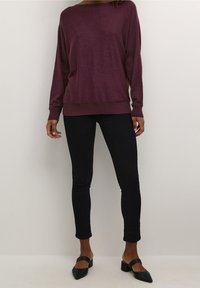 Kastanjebrun långärmad tröja med bred krage, kombinerad med svarta skinny jeans och svarta klackskor. Mjuk textur, avslappnad passform.