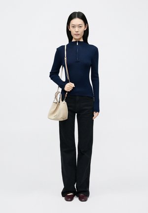 Maglia a coste blu navy a maniche lunghe con collo alto e cerniera parziale, abbinata a pantaloni neri a gamba larga e una borsa beige chiaro.