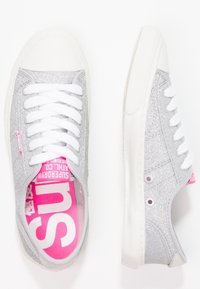 Sneaker glitterati argento con lacci bianchi e suole in gomma. L'interno rosa presenta il marchio "SUPERGA". Design con punta arrotondata, a profilo basso.