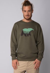 Olivegrüner Sweatshirt mit langen Ärmeln, das eine Bärensilhouette zeigt, die mit Wald- und Bergdesigns in Türkis und Dunkelgrün gefüllt ist.