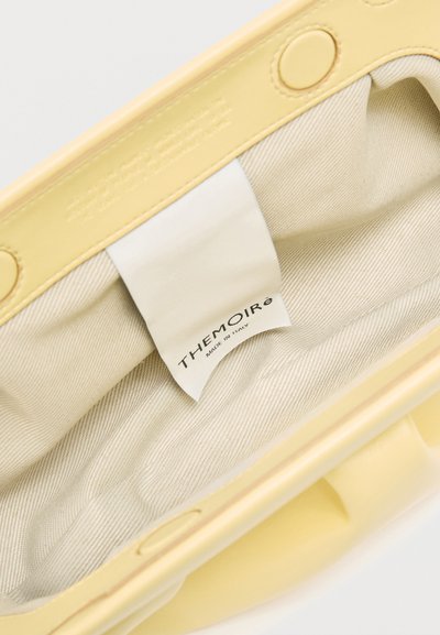 Intérieur en tissu crème d'un sac à main jaune clair avec une étiquette de marque Themioré blanche cousue à l'intérieur.