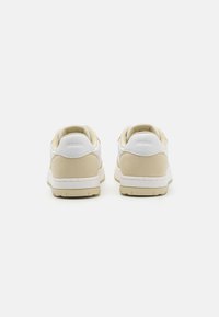 White and beige sneakers with a suede upper, padded collar, rubber sole, and contrasting heel accent. Simple, low-top design.