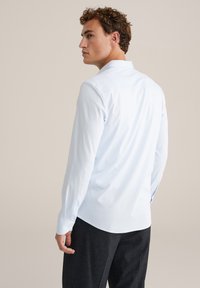 Lichtblauw overhemd met lange mouwen, een standaardkraag, knoopmanchetten en een gladde textuur. Heeft een afgeronde zoom en een detail met een achterkant yoke.