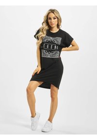 Czarna sukienka T-shirt z graficznym nadrukiem w paisley. Krótkie rękawy i lekko zaokrąglony dół. Noszona z białymi sneakersami.