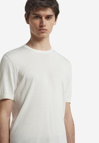 Kortärmad vit stickad tröja med rund halsringning, slät struktur och ribbade muddar, designad för en figurnära passform.