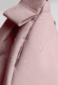 Borsa di stoffa rosa con una superficie texturizzata e una parte superiore piegata. Gocce d'acqua sono visibili sul materiale, indicando resistenza all'acqua.