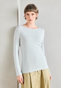 Blusa de manga longa azul claro em textura canelada com decote redondo, combinada com uma saia caqui. Design simples e ajustado.