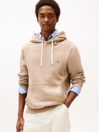 Felpa in cotone beige con tasca frontale, lacci bianchi e piccolo logo. Indossata sopra una camicia a righe blu e bianche con colletto.